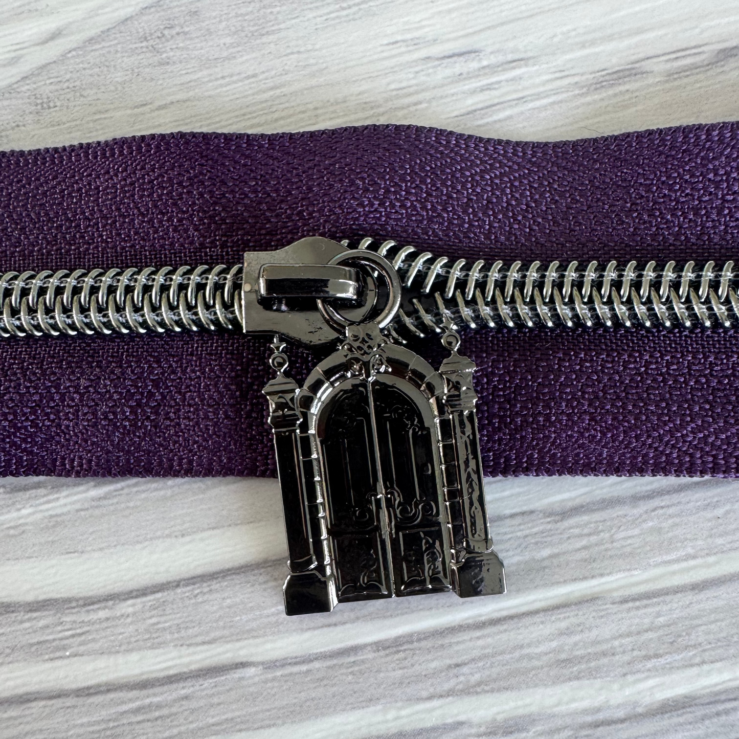 Decorative zipper pull on a purple zipper against a marble background