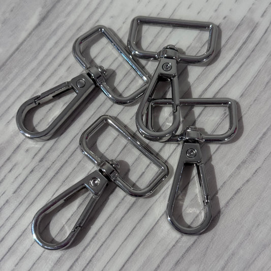 Four shiny silver metal swivel snap hooks with rectangular loops, arranged on a light gray wood-textured surface.