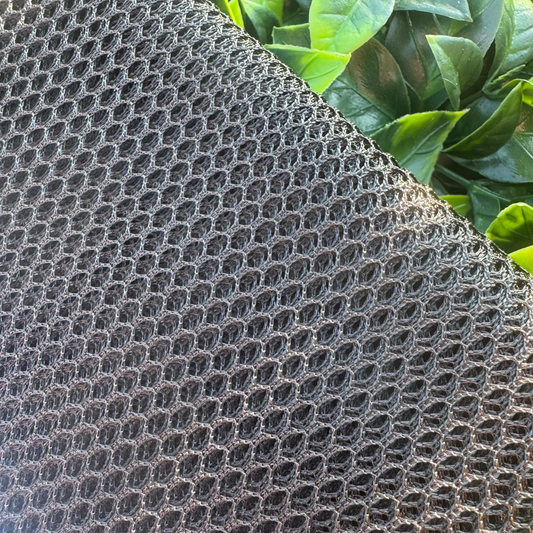 Textured black material with a honeycomb pattern against a green leafy background