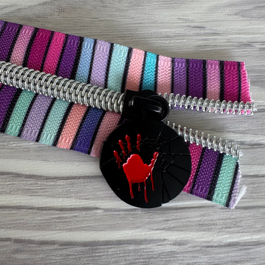 Colorful striped belt with a black buckle featuring a red handprint on a wooden surface.