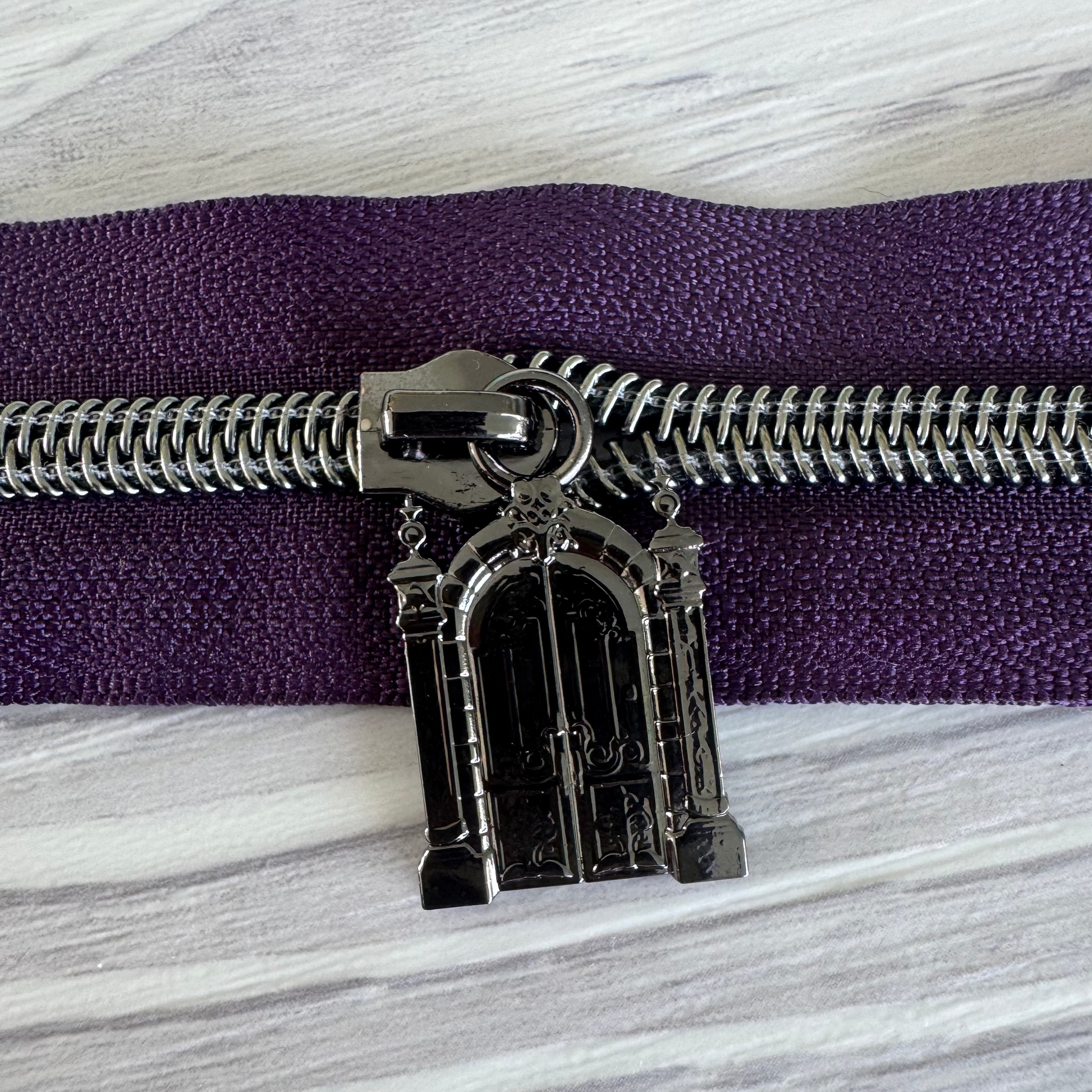 Decorative zipper pull on a purple zipper against a marble background
