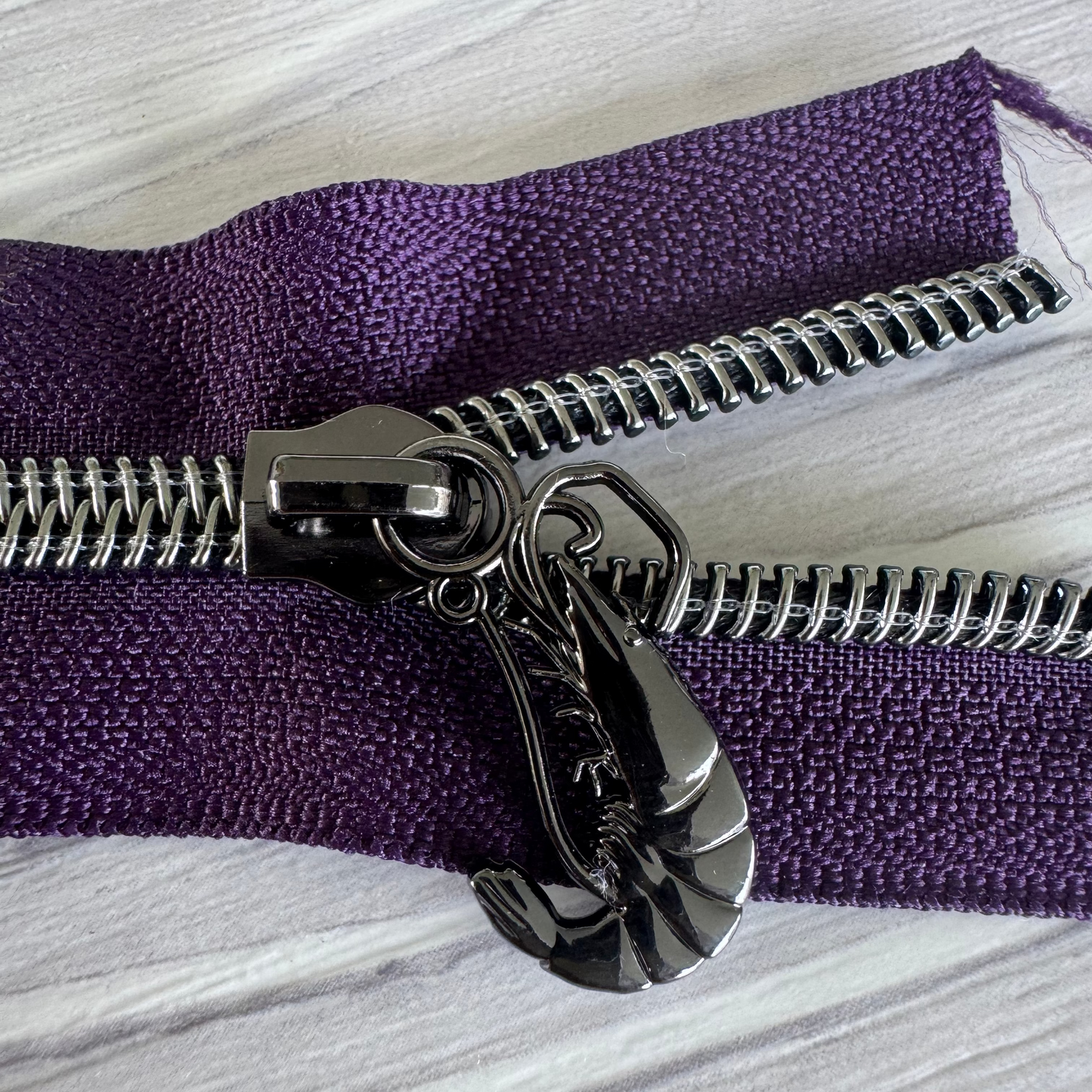 Close-up of a purple fabric with a silver zipper on a gray surface